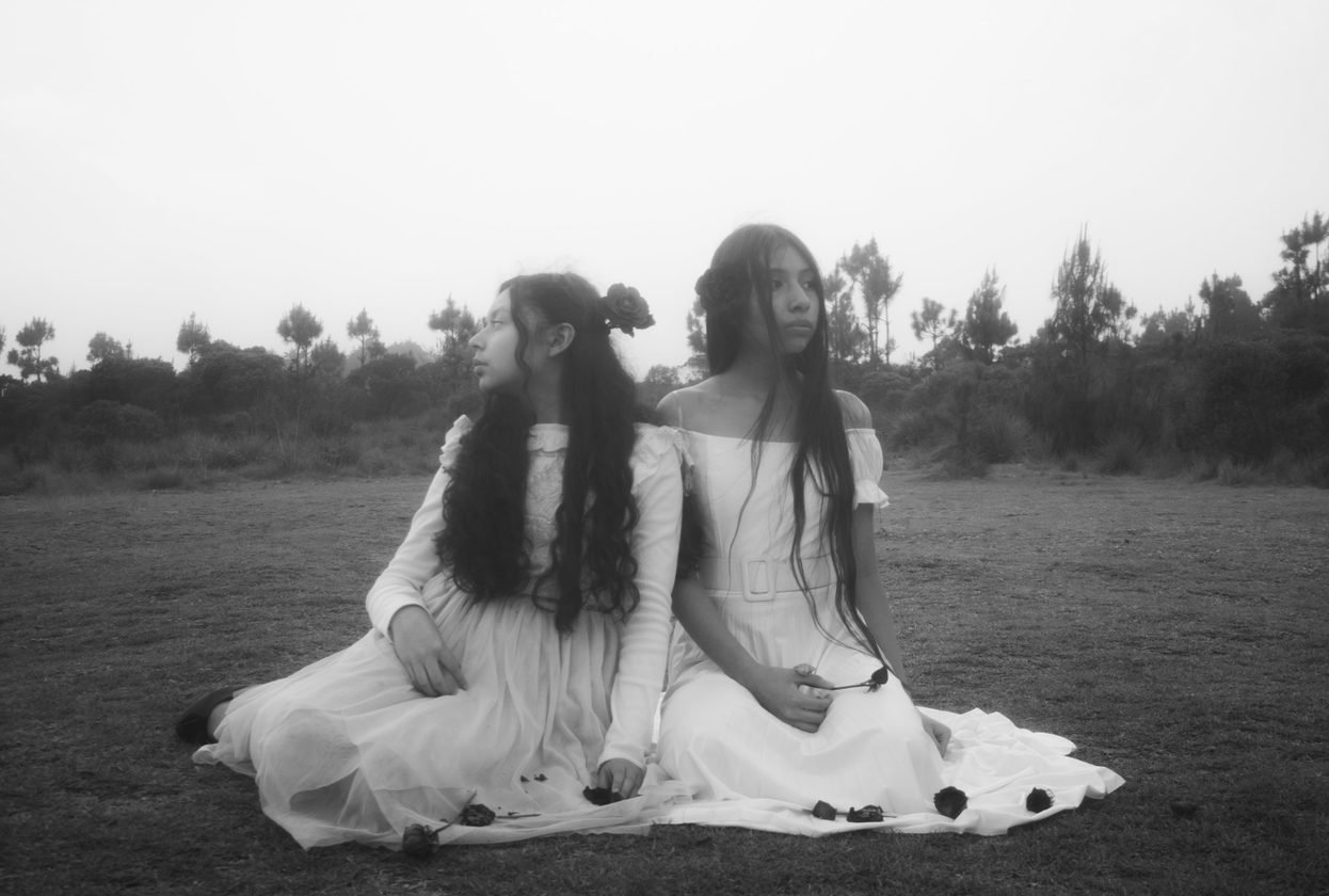 Dos jóvenes con vestidos blancos sentadas en un campo con niebla