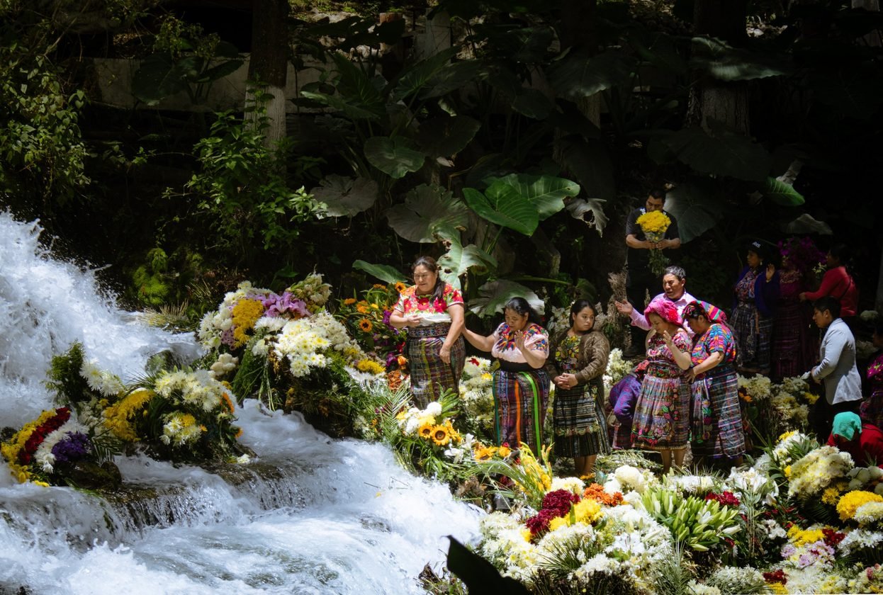 Mujeres con trajes tradicionales entre flores junto a una cascada