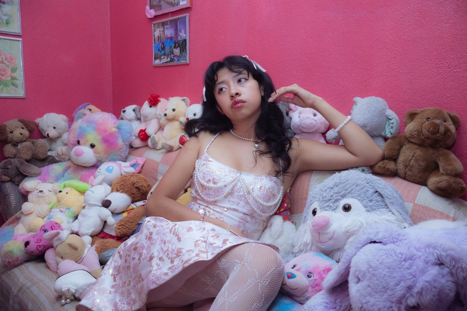 Joven con vestido floral sentada entre peluches sobre una pared rosa